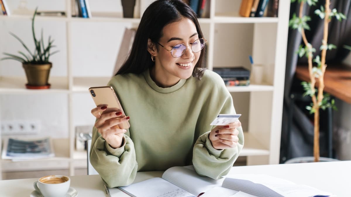 Woman smiling while holding a phone and credit card at a desk with an open notebook, exploring 0% intro APR credit cards.